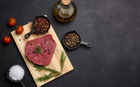 肉木板摄影照片_一块生牛肉，配香料胡椒、迷迭香小枝、盐和橄榄油，放在木板上，黑色背景。