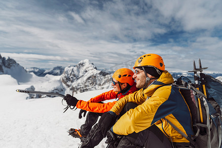 阳光明媚的日子里，两名穿着冬季远足装备的微笑徒步旅行者坐在雪地里，在高山上的侧视图