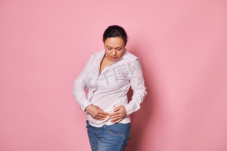 粉红色孕妇摄影照片_自信的孕妇穿上骨科腹部支撑绷带，隔离在粉红色背景中