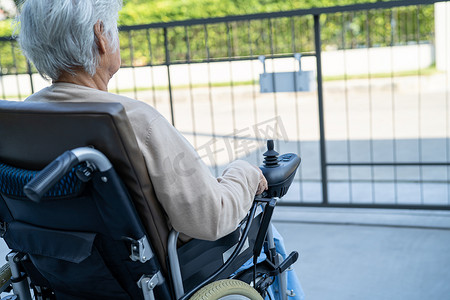 亚洲老年女性患者在医院远程控制电动轮椅，健康强大的医疗理念。