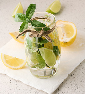 小柠檬水摄影照片_透明玻璃杯中的柠檬水，白色背景上有柠檬、酸橙、迷迭香小枝和薄荷叶