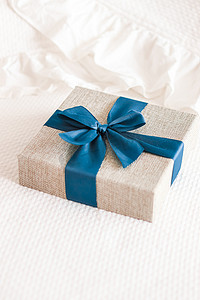 假日礼物和豪华网上购物送货，卧室床上带蓝丝带的包裹亚麻礼盒，别致的乡村风格