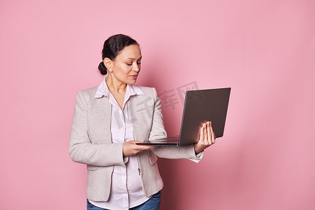 自信的中年黑发女性、程序员、企业主、销售经理、使用笔记本电脑的招聘人员、粉红色背景