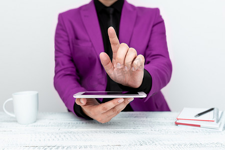 穿着粉红色夹克的商人坐在桌旁拿着手机，用一根手指指着重要信息。