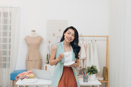 美丽的年轻亚洲时装设计师女商人在她的工作室喝咖啡时的肖像