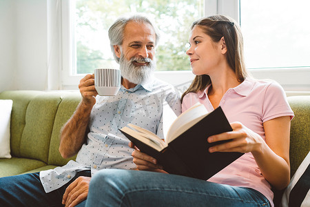 微笑的老人喜欢和孙女在一起，坐在他旁边的年轻女人拿着一本书