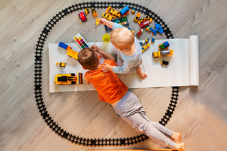 学龄前男孩在纸上画画，玩益智玩具——积木、火车、铁路、家里的车辆或托儿所。