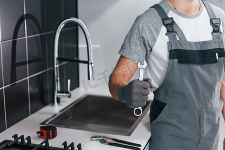 在厨房里手拿扳手的灰色制服年轻专业水管工的特写镜头