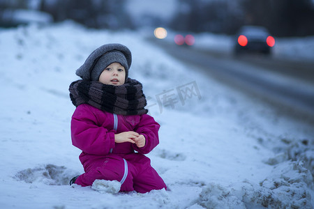 一个小女孩坐在路边的雪地里，看着过往的车辆