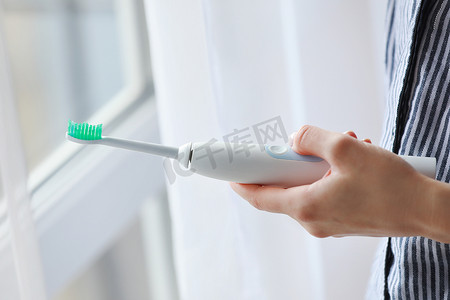 牙刷背景摄影照片_在家里使用电动牙刷的女人。
