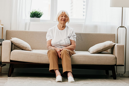 老年妇女坐在沙发上剧烈腹痛，老年健康问题，生活质量差。