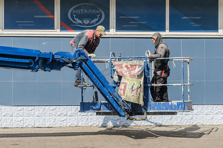 白俄罗斯，博布鲁伊斯克 — 2020年9月2日：两名在城市一家商店正面附近的升降平台上工作的建筑工人拆除旧广告