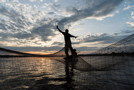 渔民在日落时分在 W 抛网捕鱼的剪影