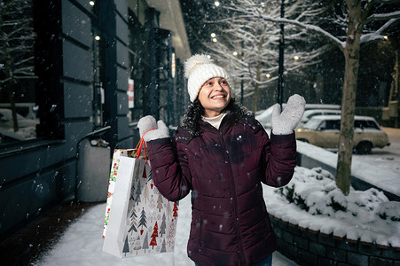 带着购物袋走在积雪覆盖的街道上时，可爱的年轻女人抓着雪花