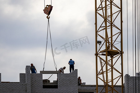 工队摄影照片_一队建筑工人和一台起重机在傍晚多云的天空背景下建造建筑物。