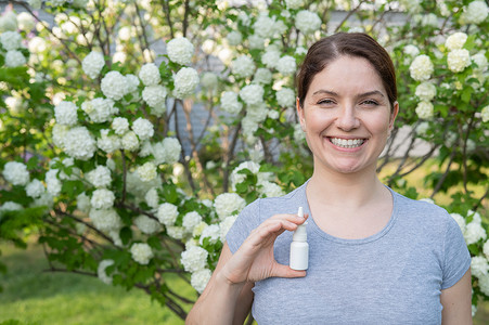 幸福的女人在一棵开花的树的背景下展示喷鼻剂。
