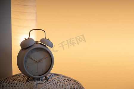 篮子的柳条盖上立着一个模拟闹钟，背景是点亮的床头灯。