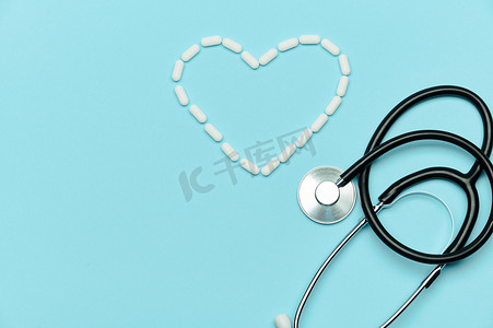 心脏蓝色背景摄影照片_医生听诊器和药丸以心脏的形式布置在蓝色背景上。