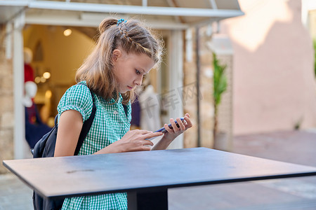 10 岁、11 岁的女童在城市里拿着智能手机。