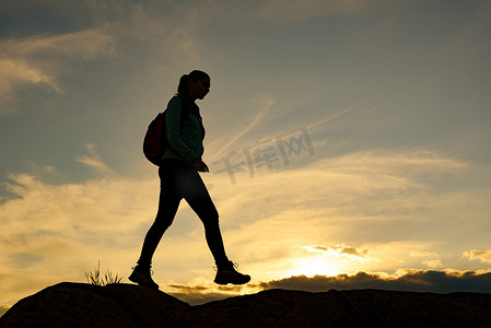 年轻女子旅行者在夏季日落时背着背包在美丽的岩石小径上徒步旅行。