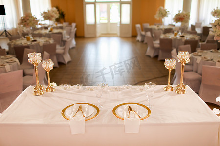 企业餐厅摄影照片_餐厅的餐桌装饰有粉色桌布、带蜡烛的水晶烛台和白色粉色花朵。