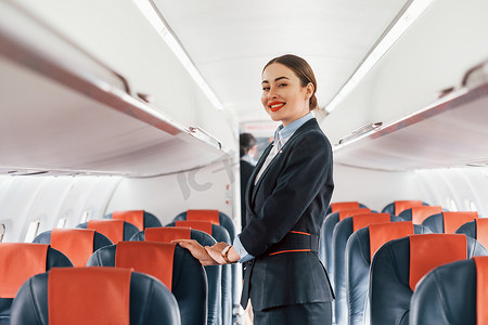 黑色衣服的人摄影照片_穿着正式的黑色衣服的年轻空姐站在飞机的室内