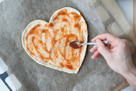 厨师心摄影照片_心形披萨面团，厨师在披萨上涂上番茄酱。