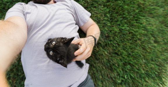 宠物主人摄影照片_横幅男子用智能手机自拍，小猫躺在草地上玩耍 — 友谊爱动物和宠物主人的概念