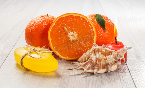 用两个完整的橙子、肥皂、贝壳和燃烧的蜡烛切橙子。