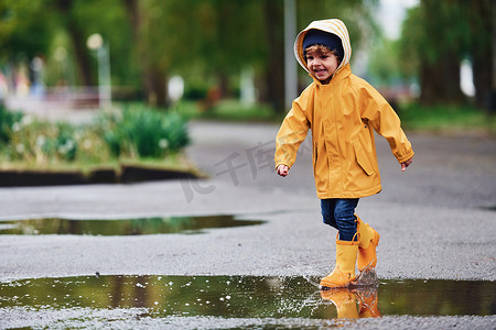 孩子斗篷摄影照片_雨后穿着黄色防水斗篷和靴子在户外玩耍的孩子