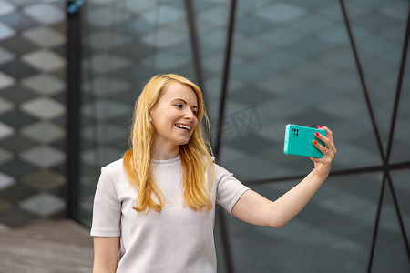 年轻的金发女人在智能手机上为她的追随者自拍。