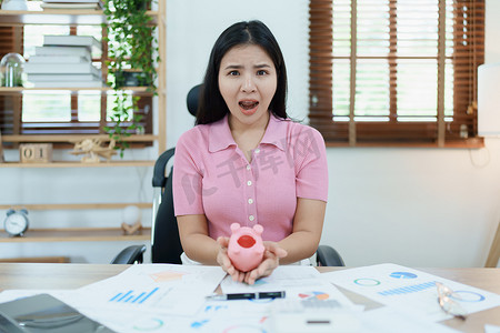 一位亚洲女商人在中小企业业务中表现出严肃而焦虑的表情，但粉红猪存钱罐里没有钱，储蓄计划