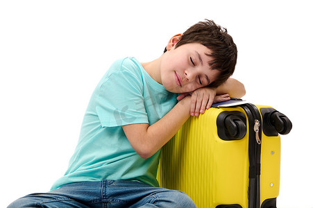 一个可爱的十几岁男孩在黄色手提箱上睡着的白色背景上的孤立肖像。