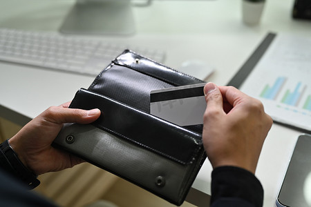 钱包银行卡摄影照片_拿着塑料银行卡和黑色皮革钱包的人的特写镜头。