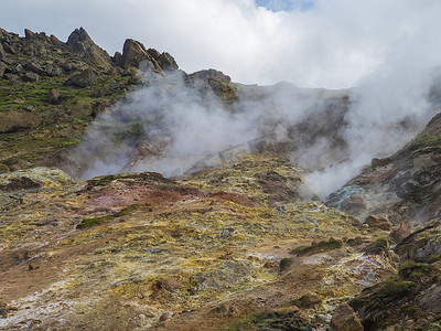 Reykjadalur 山谷的彩色流纹岩红色、橙色和黄色喷气孔，有锋利的岩石、草地和地热蒸汽。 