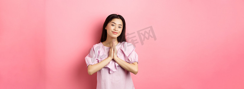 敬礼的青少年摄影照片_可爱的亚洲女孩说谢谢，微笑着，看起来很开心，表现出合十的手势表示感谢，穿着粉色背景的裙子
