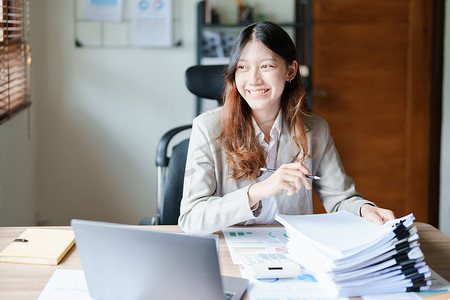 财务报表摄影照片_财务、规划、营销和会计，亚洲员工在工作中使用文件和笔记本电脑检查财务报表的肖像