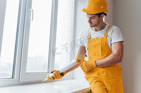 身穿黄色制服的杂工在室内使用窗户胶水。