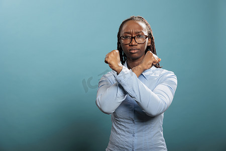 不手势摄影照片_站在蓝色背景上，不赞成非洲裔美国妇女用交叉双臂做停止手势。