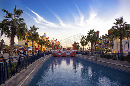 阿联酋迪拜 — 2020 年 12 月 16 日，在阿联酋迪拜地球村的傍晚日落时间，公园娱乐中心的国家馆和运河以及游船的美丽景色。