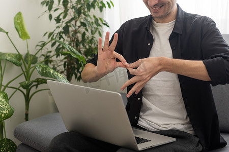 学手语摄影照片_年轻人用笔记本电脑用手语显示手势，进行视频通话