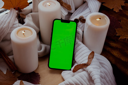 绿屏 chromakey 手机应用程序在审美氛围背景下复制空间秋叶香料和蜡烛在温暖的黄色灯光下针织白色毛衣。