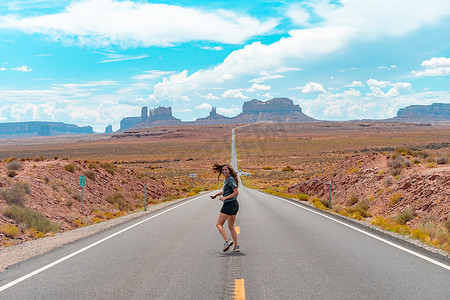 公路奔跑摄影照片_从后面看有魅力的年轻女人在沙漠中的美国直路中间奔跑。