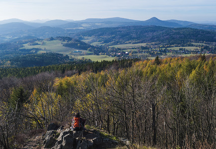 年轻女子徒步旅行者从 Hochwald Hvozd 的 Lusatian 山脉的观点拍摄 Luzicke hory 全景照片，秋季色彩斑斓的落叶和针叶林和青山，黄金时段的灯光