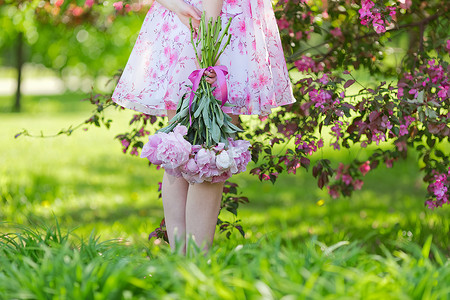 捧花的女孩摄影照片_一个穿着粉红色连衣裙的女孩，手捧一大束牡丹
