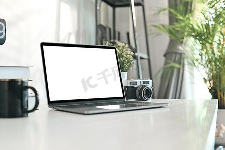 创意设计师工作场所，白桌上配有笔记本电脑、复古相机和咖啡杯