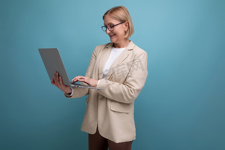 身穿夹克、带笔记本电脑的 50 多岁商务中年女性在带复印空间的工作室背景下工作