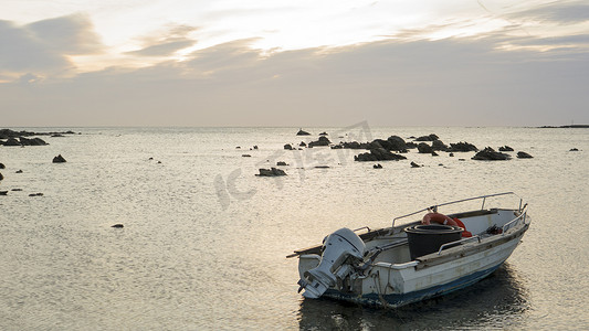 黎明时分，在一片多云的小海滩上拍摄大海的情感照片，一艘渔船停在岸边，绳索在平水中移动