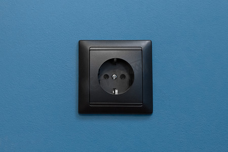 蓝墙背景上的单黑插座供电家庭能源供应电力，特写
