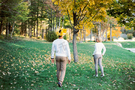 树叶花环摄影照片_戴着黄叶花环的男人跟着女人穿过秋天的公园。
